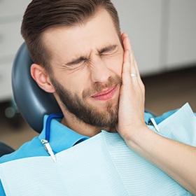 Man in dental chair holding jaw