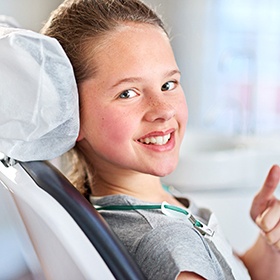 Smilihng child in dental chair giving thumbs up