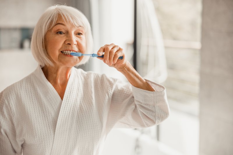 Older woman in white robe brushing teeth in bathroom